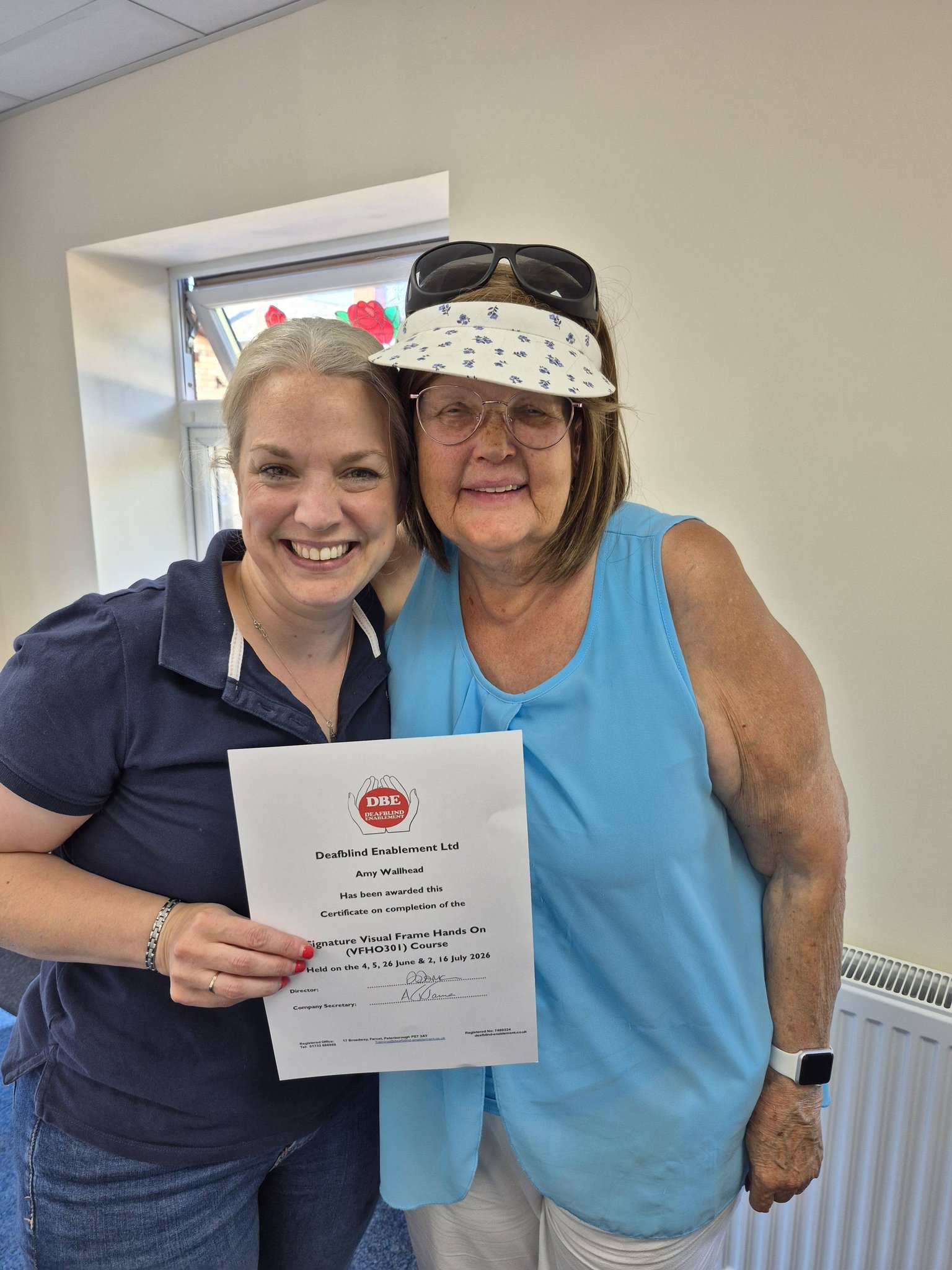 Two people smiling together and holding up a Deafblind Enablement certificate for the Signature Visual Frame Hands On course.